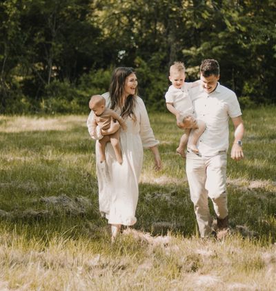 A young family walking through a sunlit meadow, each parent carrying a child