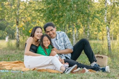 A young family sitting together on a picnic blanket in a park