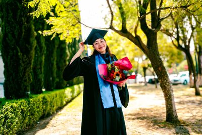 A college graduate in cap and gown holding a bouquet of flowers