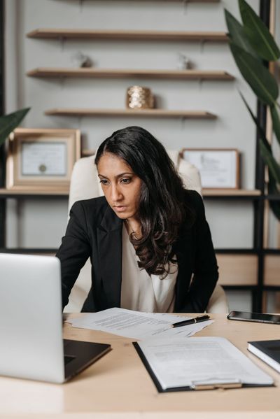 A professional reviewing documents at her desk with a laptop